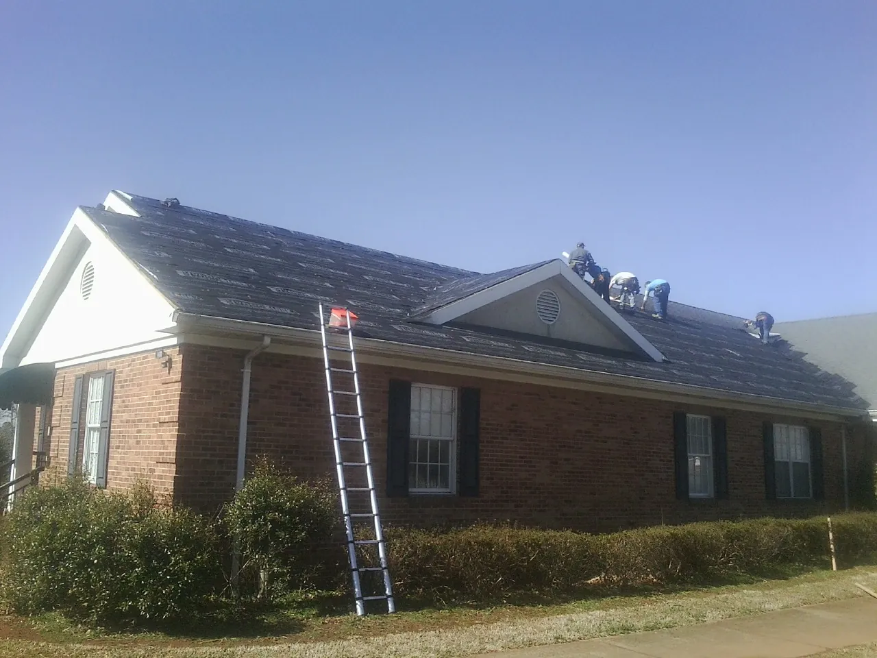 Crew tearing shingles off a brick ranch roof with a ladder set — Emergency Roof Repair work by our crew in Del Mar
