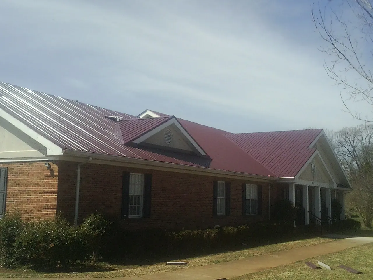 Red metal roof with gabled entries on a long brick building, from a Hail Damage Roof Repair job in Del Mar